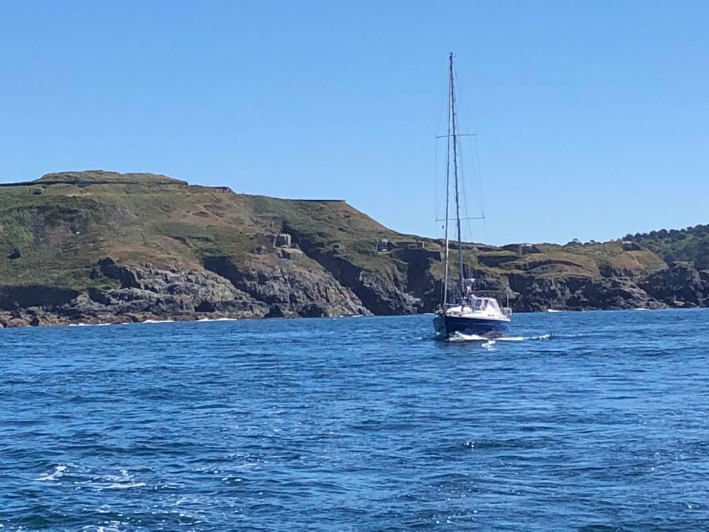 sv Phi met op de achtergrond de kust van Alderney